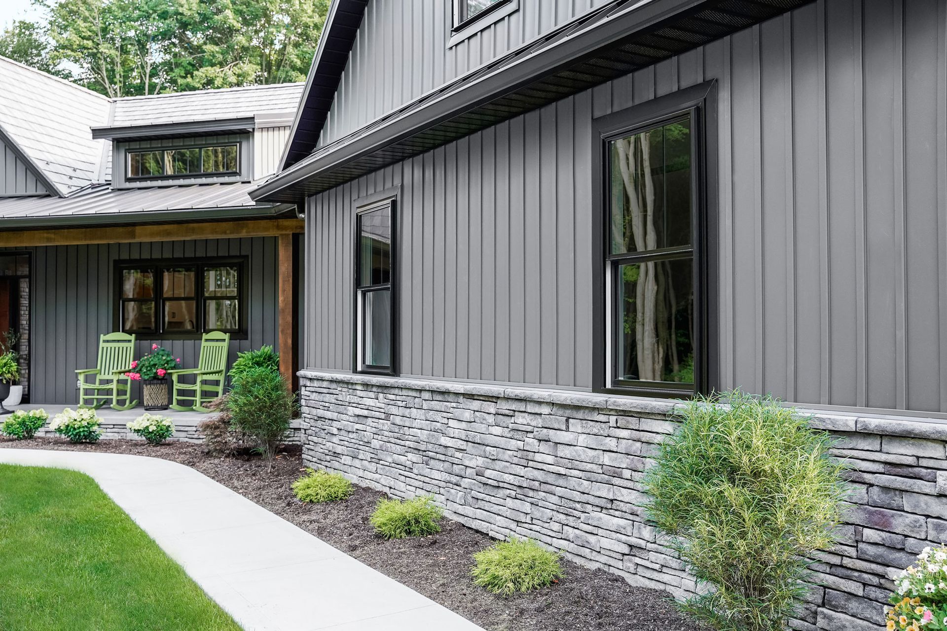 A large gray house with a stone wall and a porch.