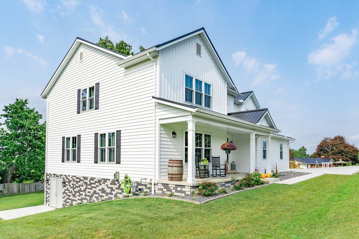 A large white house with a large porch is sitting on top of a lush green field.