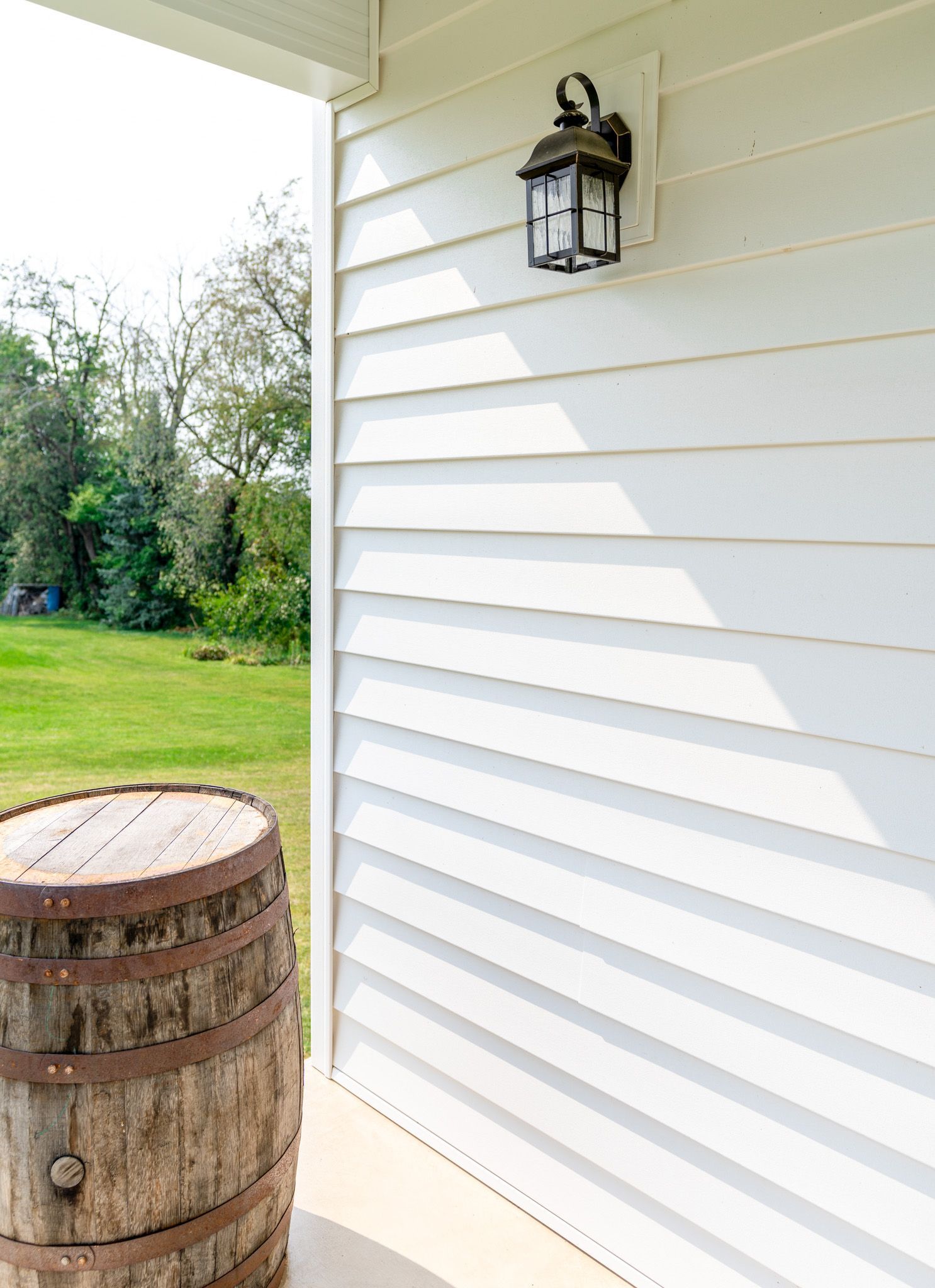 A wooden barrel is sitting on a porch next to a white house.