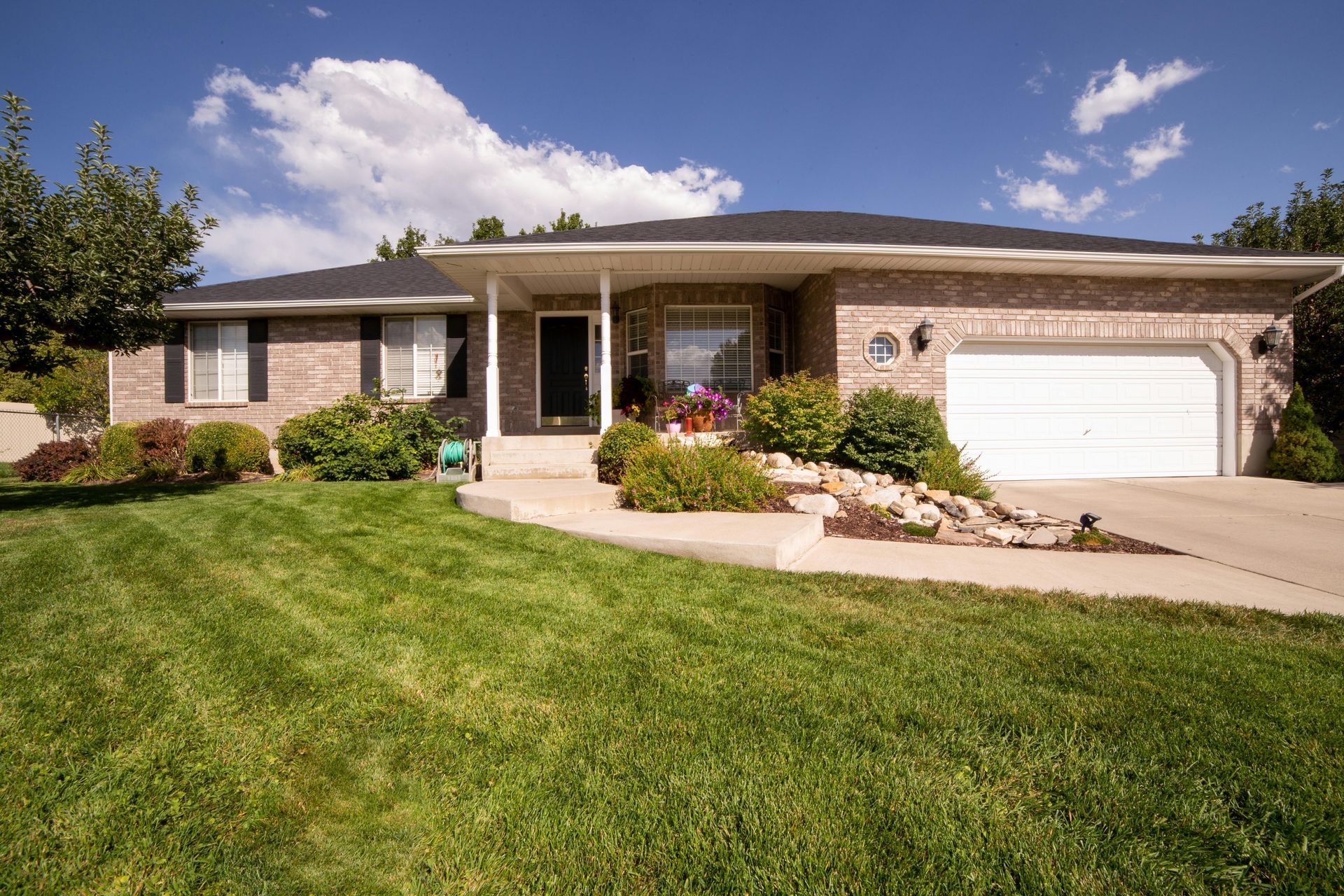 Brick ranch-style house with manicured lawn, shrubs, and a two-car garage under a blue sky.