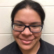 A woman wearing glasses and a black shirt is smiling.