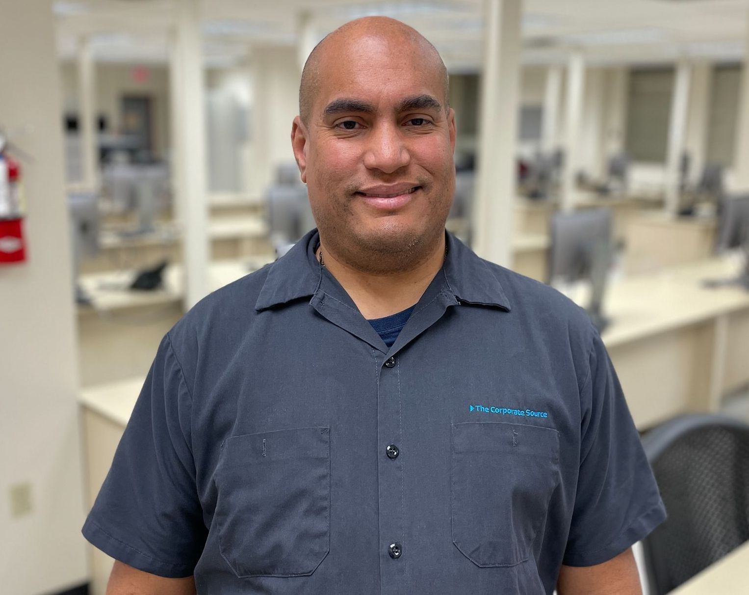 A man in a gray shirt is standing in front of a computer lab.