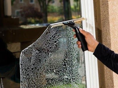 Hand using a squeegee to clean a window covered in soapy foam.