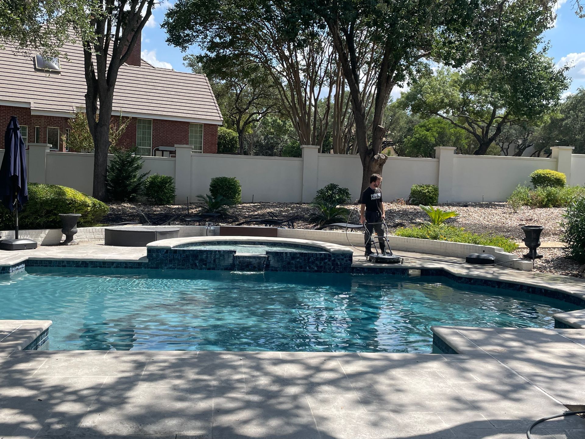 A pool with blue tile and a hot tub. A person stands near the edge with a white wall in the background.