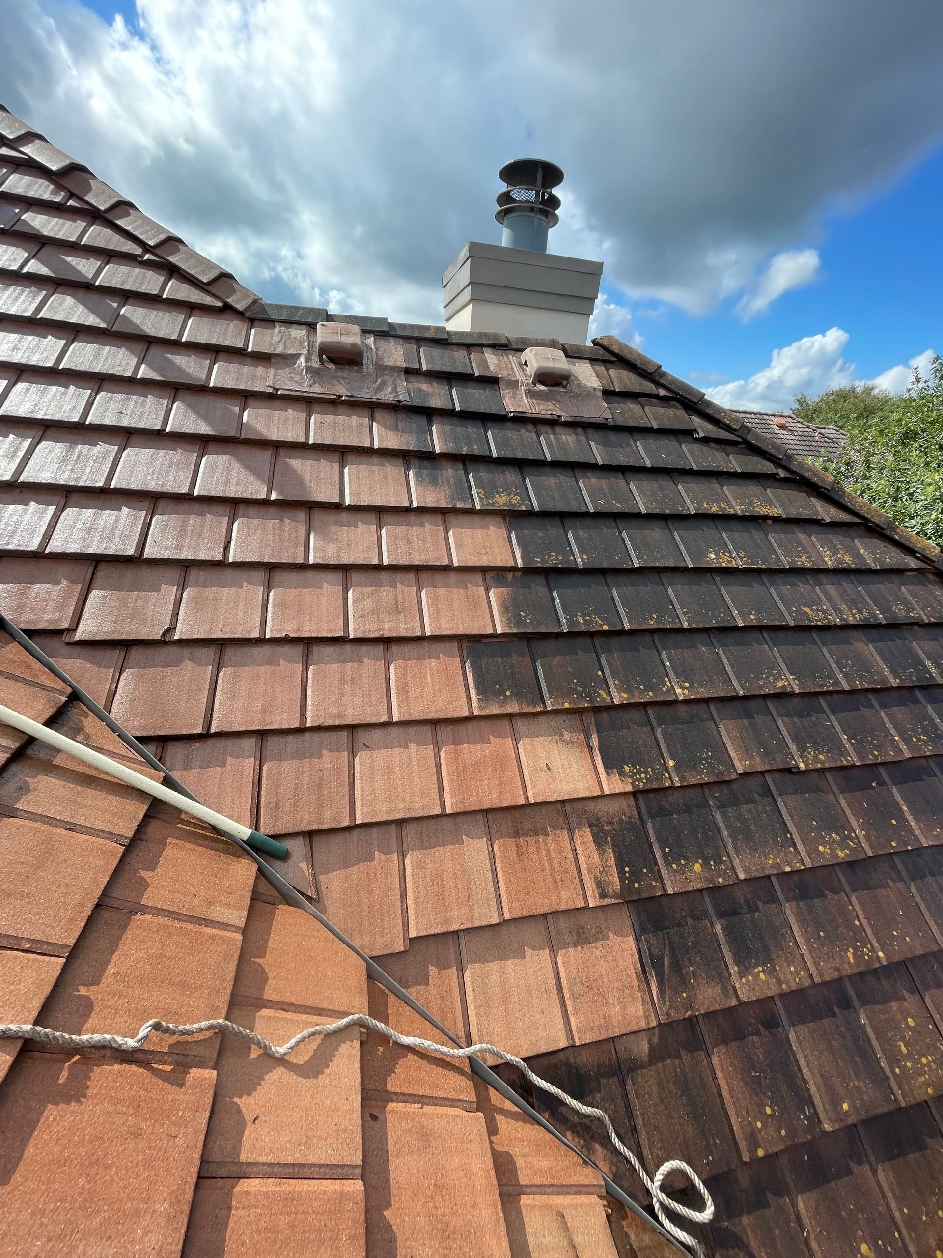 Tiled rooftop with chimney under a cloudy sky, with a rope stretched across the roof