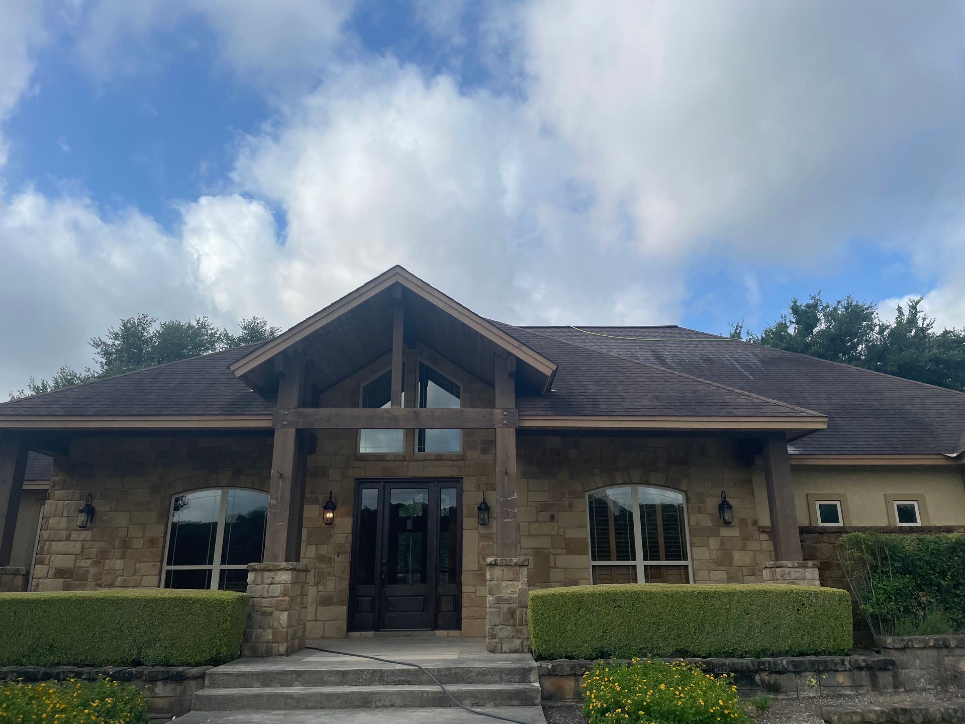 Stone building entrance with glass doors and manicured hedges under a cloudy sky