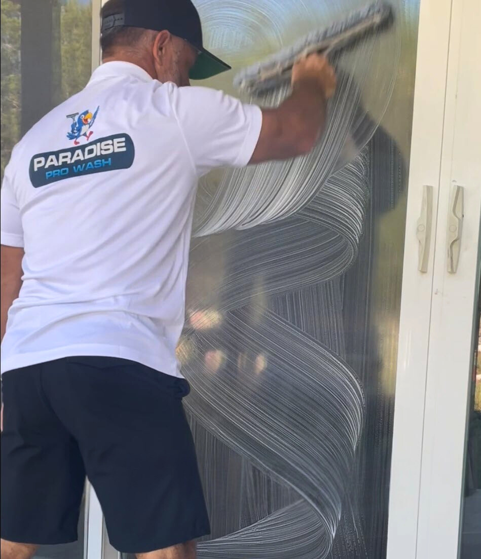 Man in white shirt with company logo cleans window with squeegee.