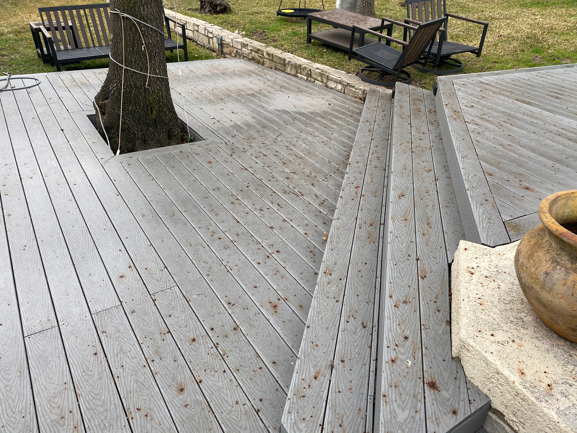 Wooden deck with steps, a tree in the center, and outdoor furniture.