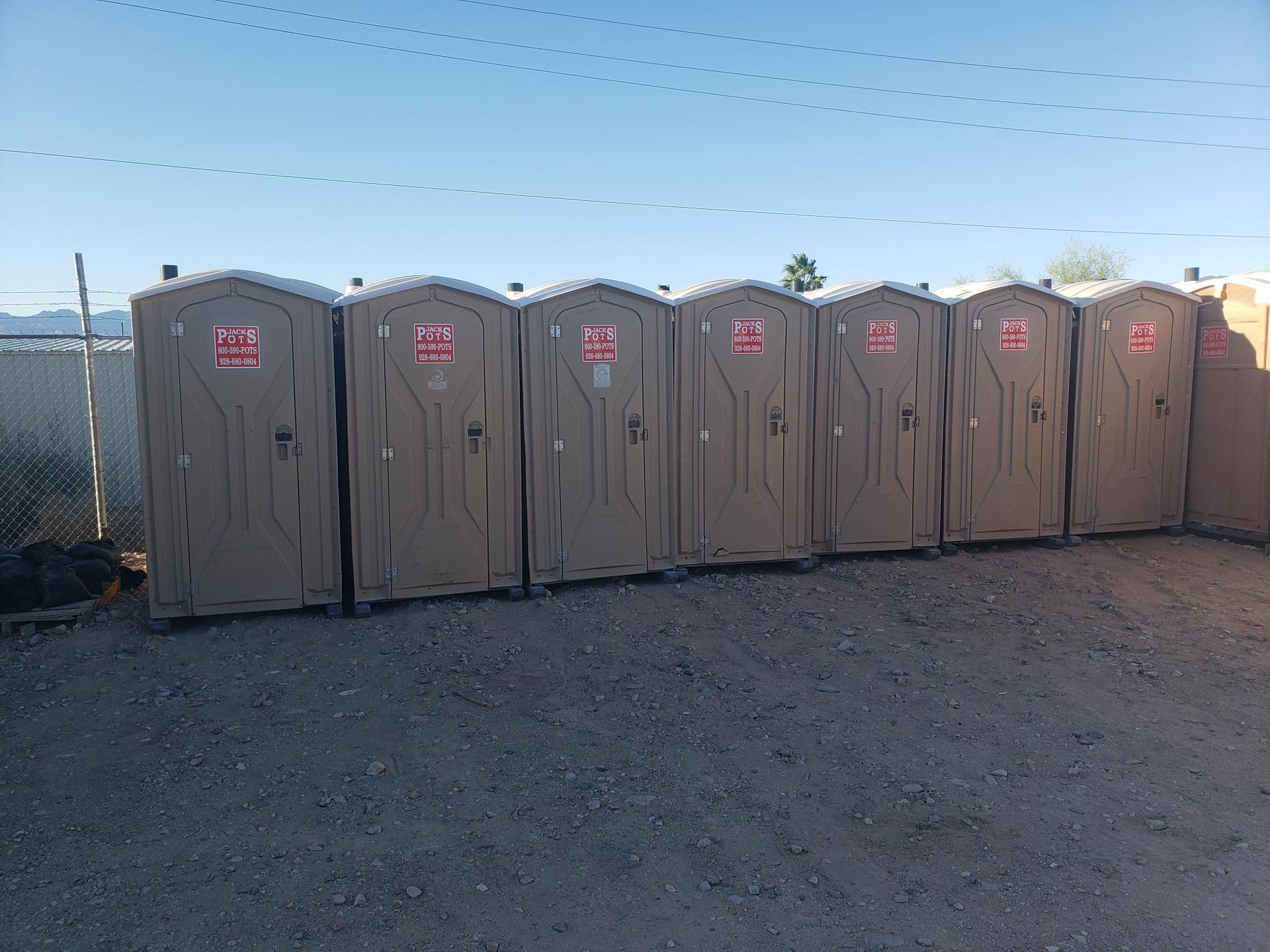 A row of portable toilets are lined up in a gravel lot.