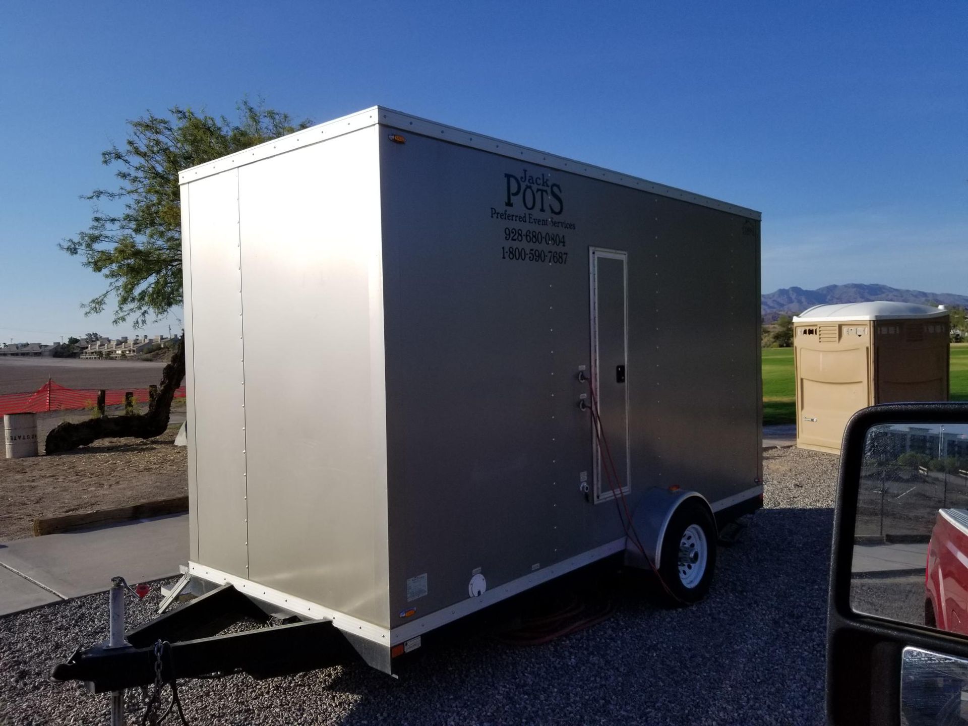 A silver trailer is parked in a gravel lot next to a truck.
