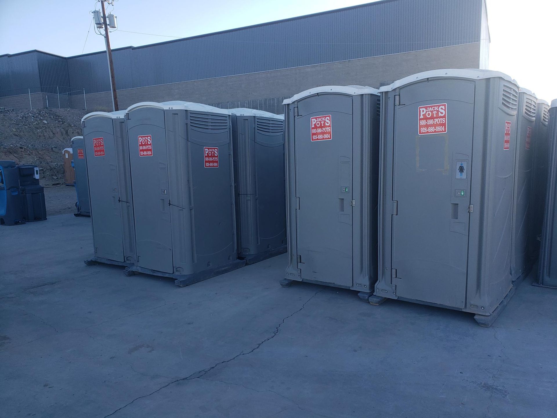 A row of portable toilets are lined up in a parking lot in front of a building.