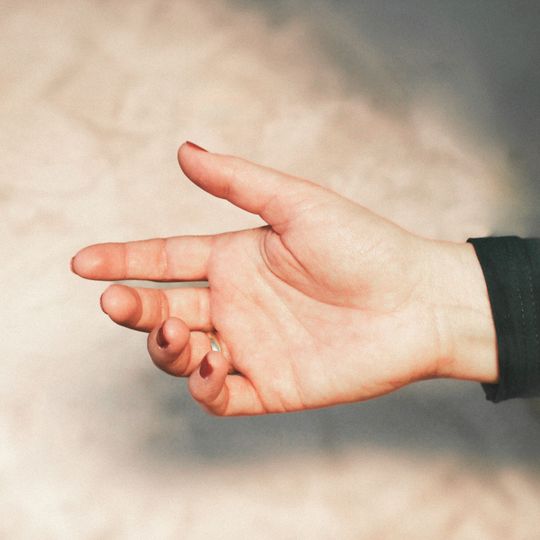 Eine hellhäutige Hand mit leicht gespreizten Fingern streckt sich vor einem weichen, hellen Hintergrund aus.