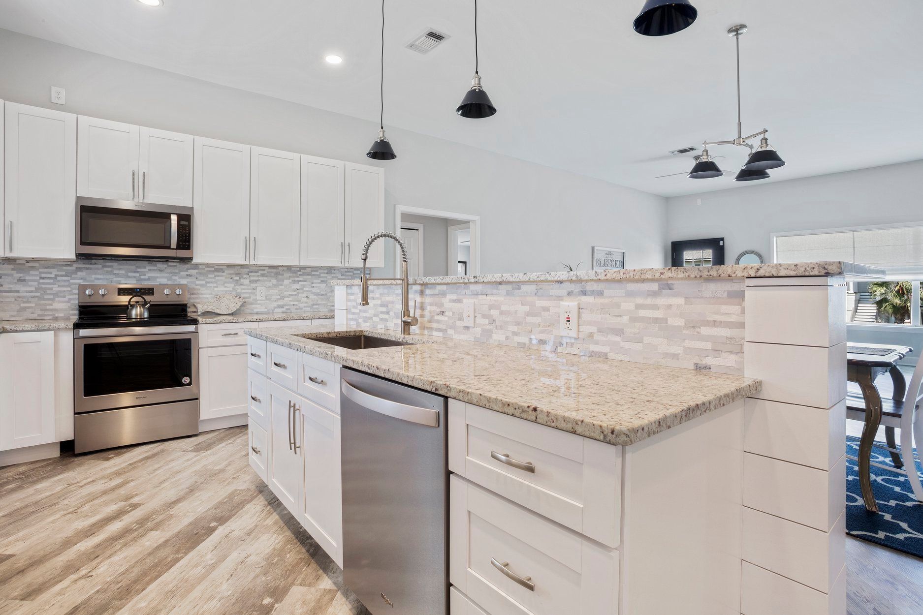 A kitchen with white cabinets , granite counter tops , stainless steel appliances and a large island.