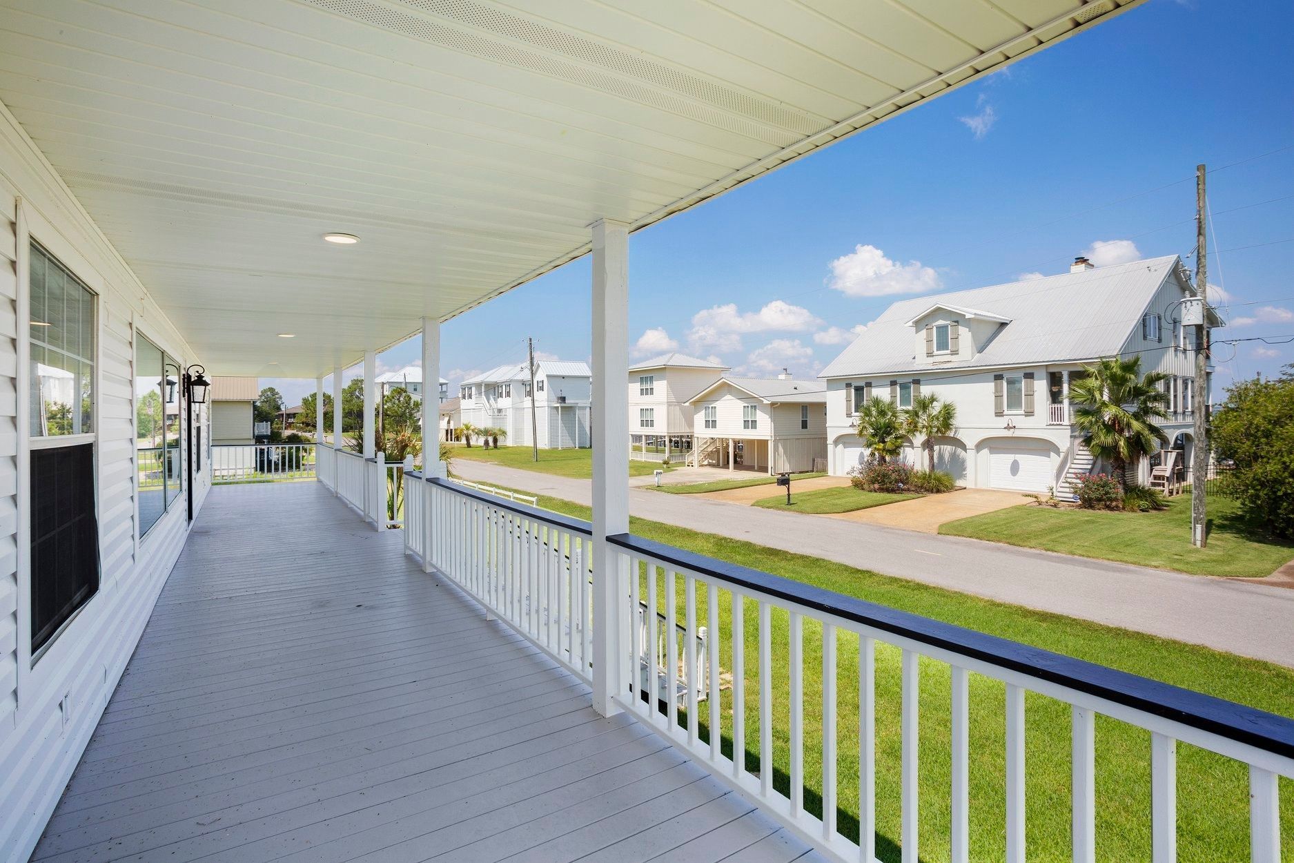 There is a large porch with a railing and a view of the street.