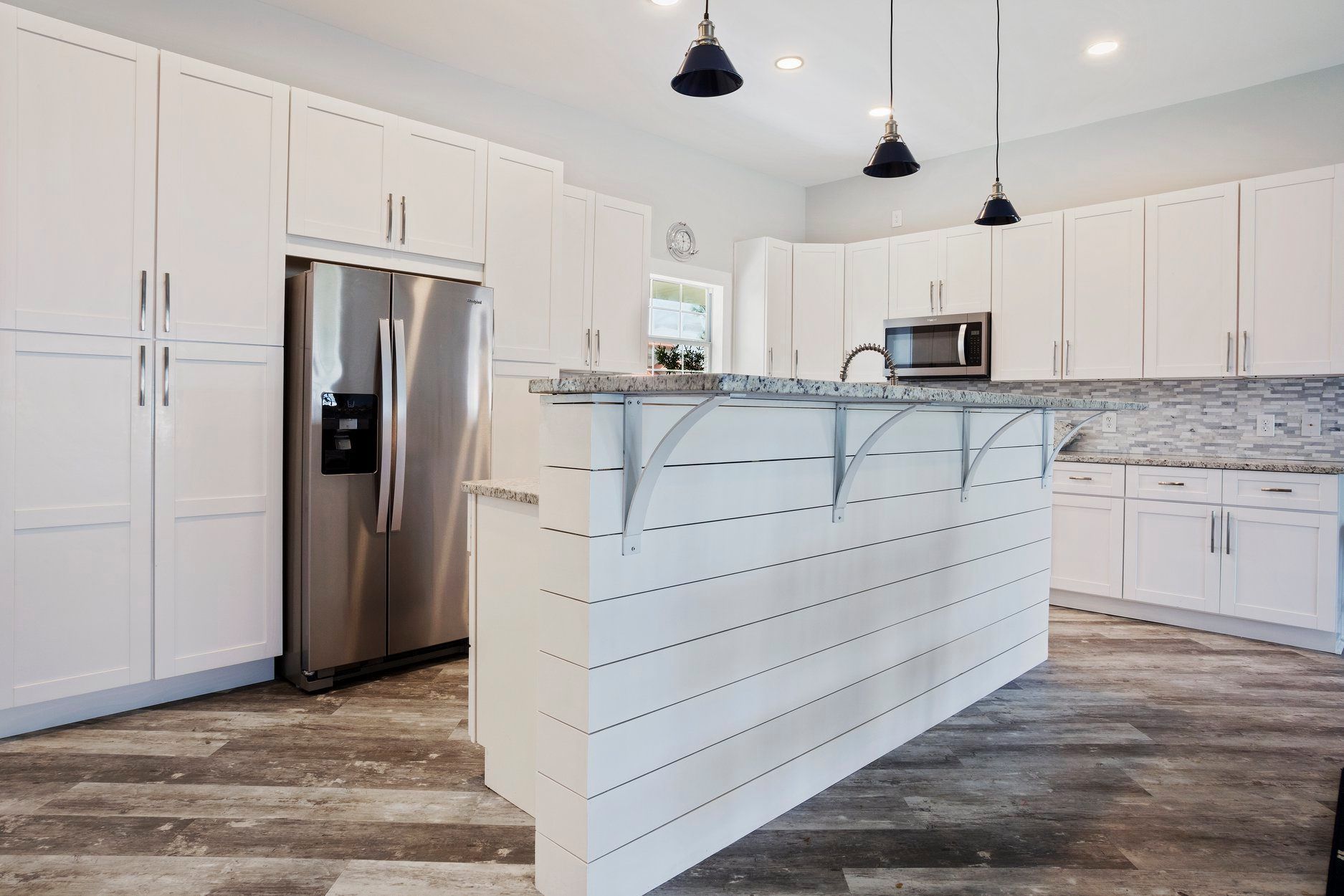 A kitchen with white cabinets , stainless steel appliances , and a large island.