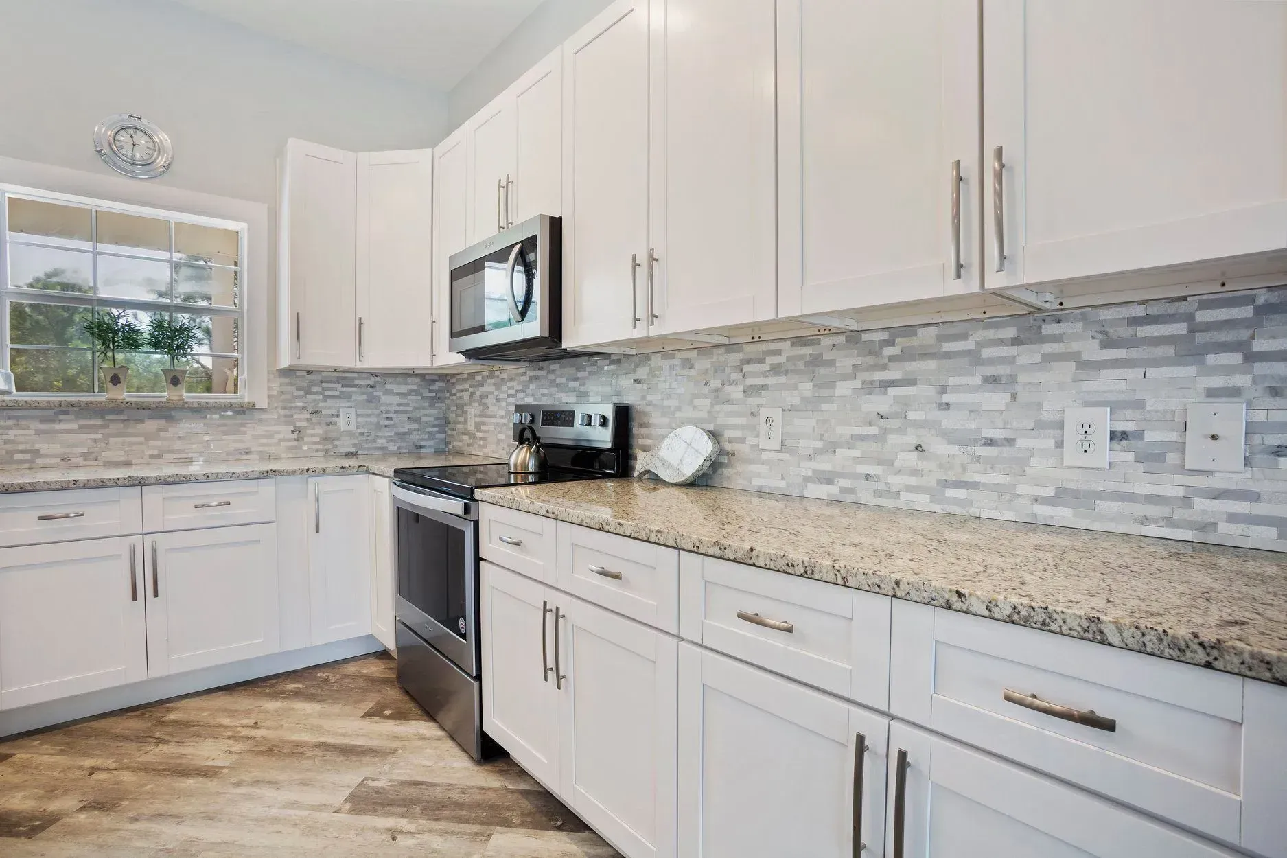 A kitchen with white cabinets , granite counter tops , and stainless steel appliances.