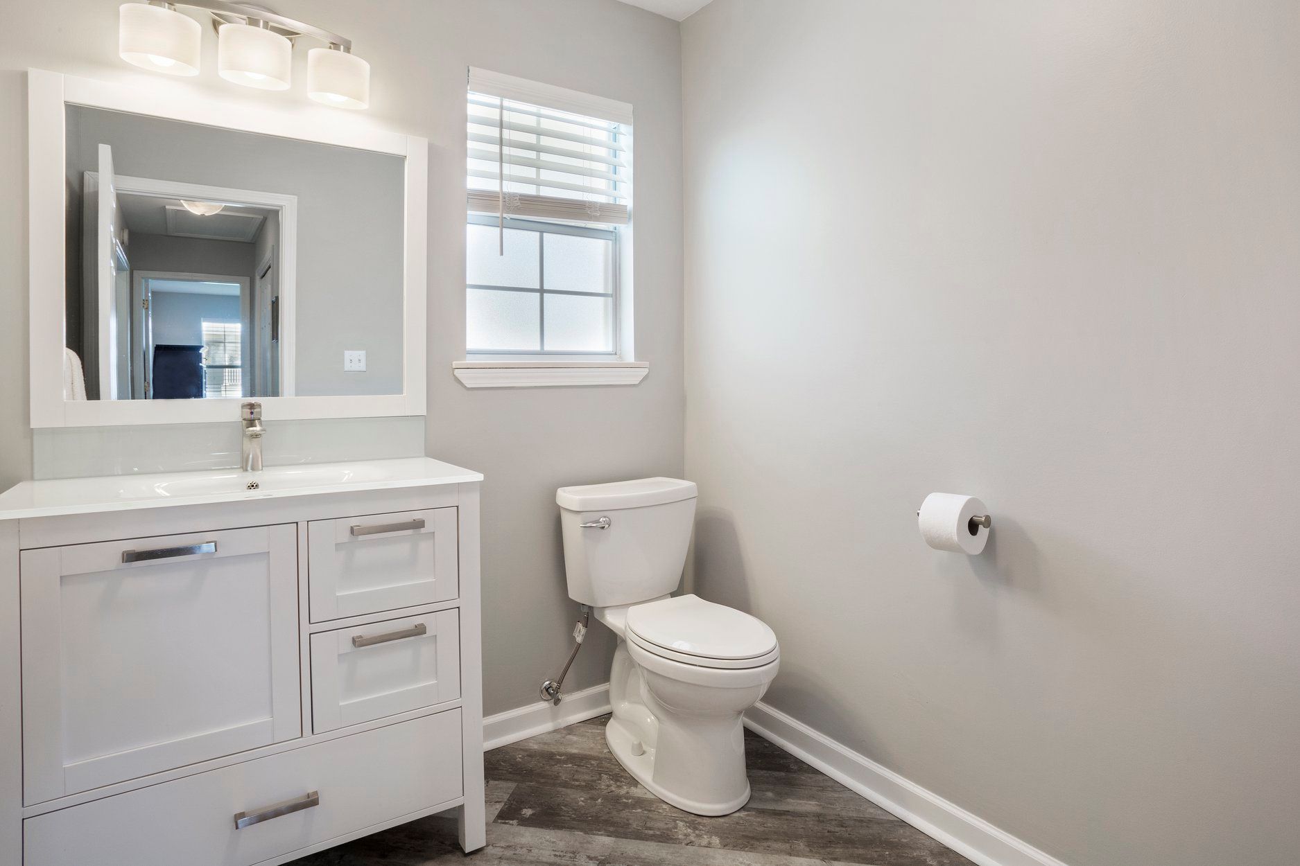 A bathroom with a toilet , sink , mirror and window.