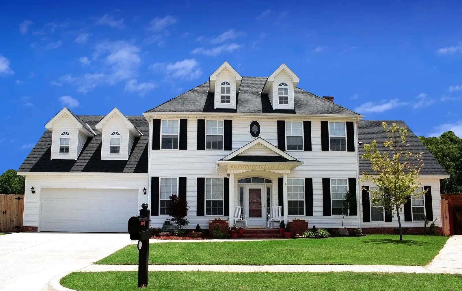 A large white house with black shutters and a mailbox in front of it