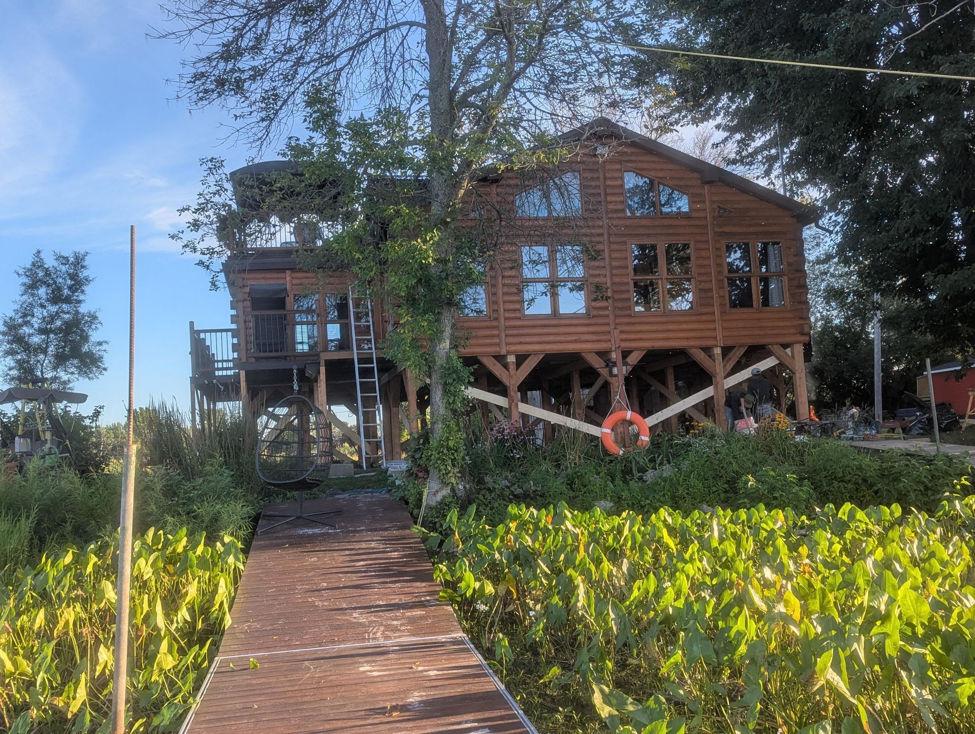 Cabane en bois sur pilotis au-dessus de l'eau, avec terrasse et quai. Un gilet de sauvetage est accroché aux supports.
