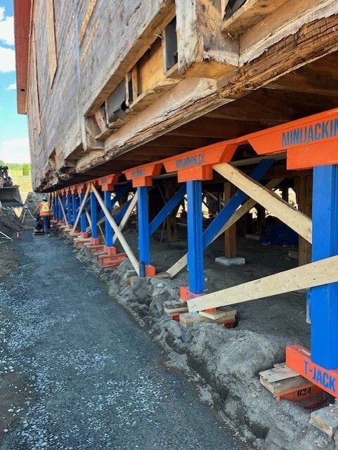 Bâtiment soulevé par des vérins structuraux bleus et orange ; chantier de construction.