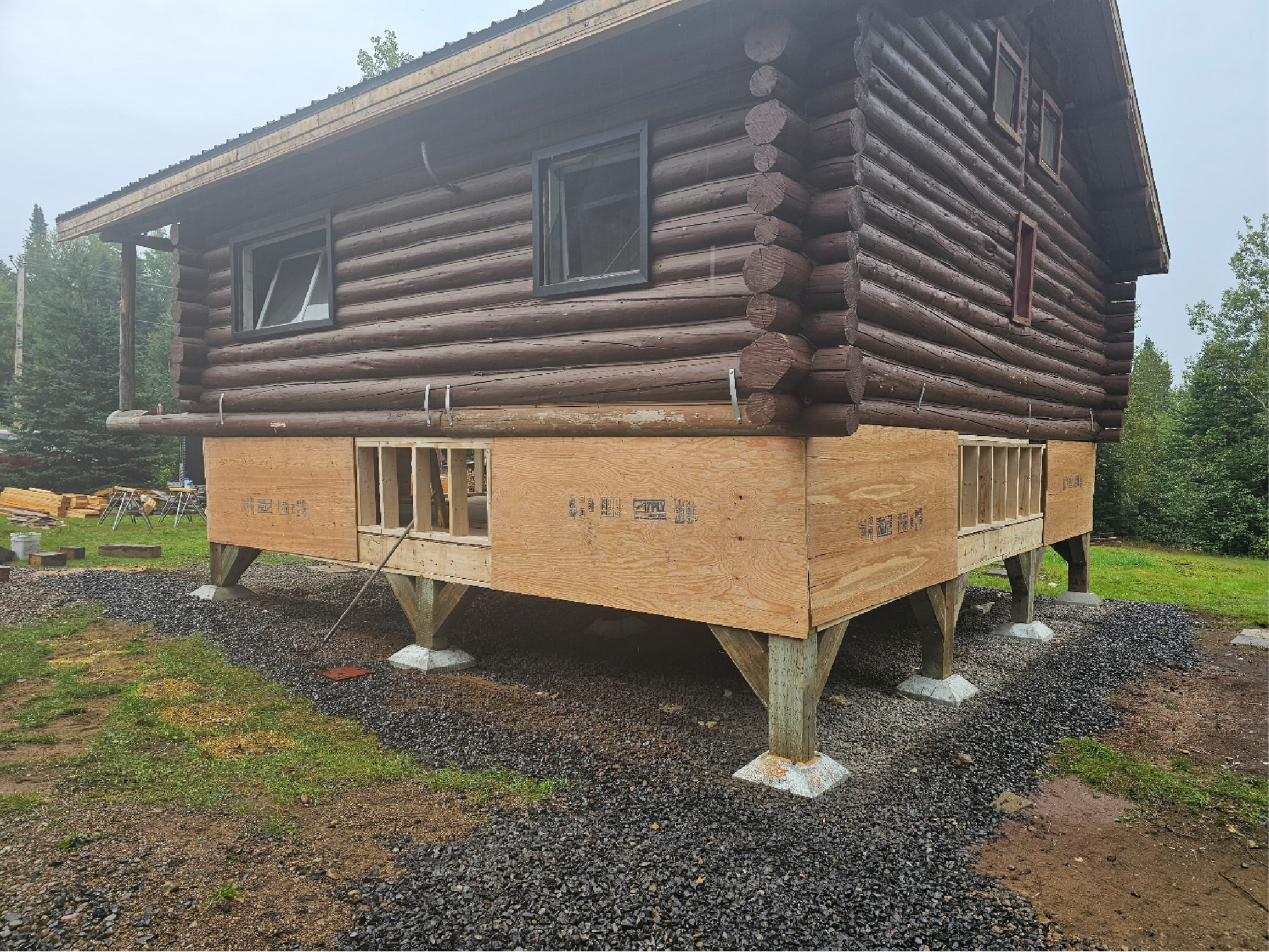 Une cabane en rondins est en cours de construction sur pilotis dans un champ.