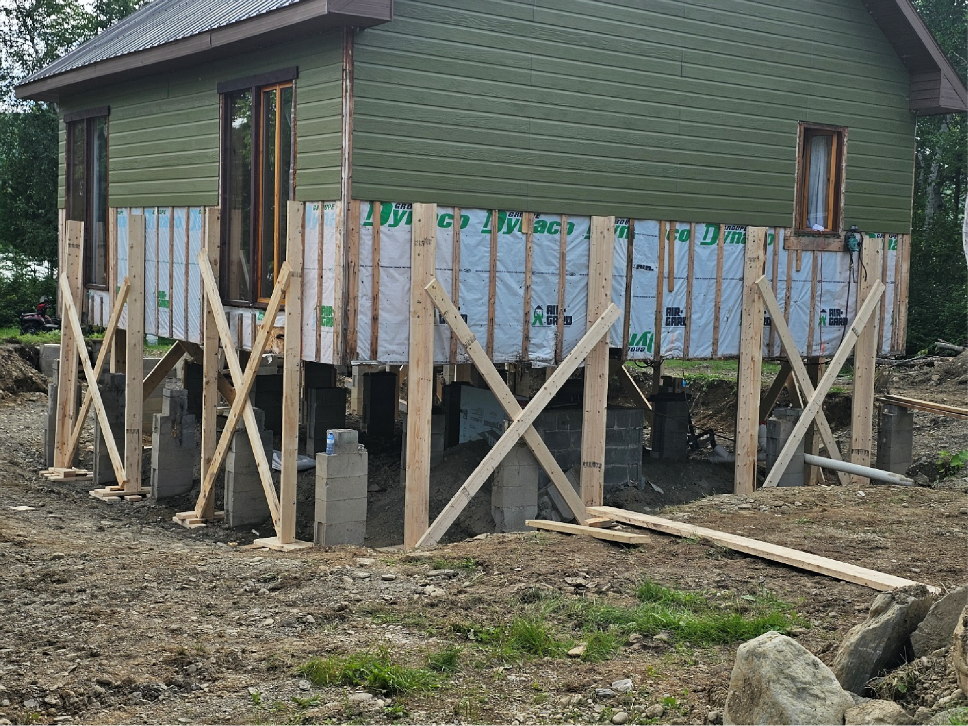 Une maison est en train d'être construite sur pilotis dans un champ de terre.