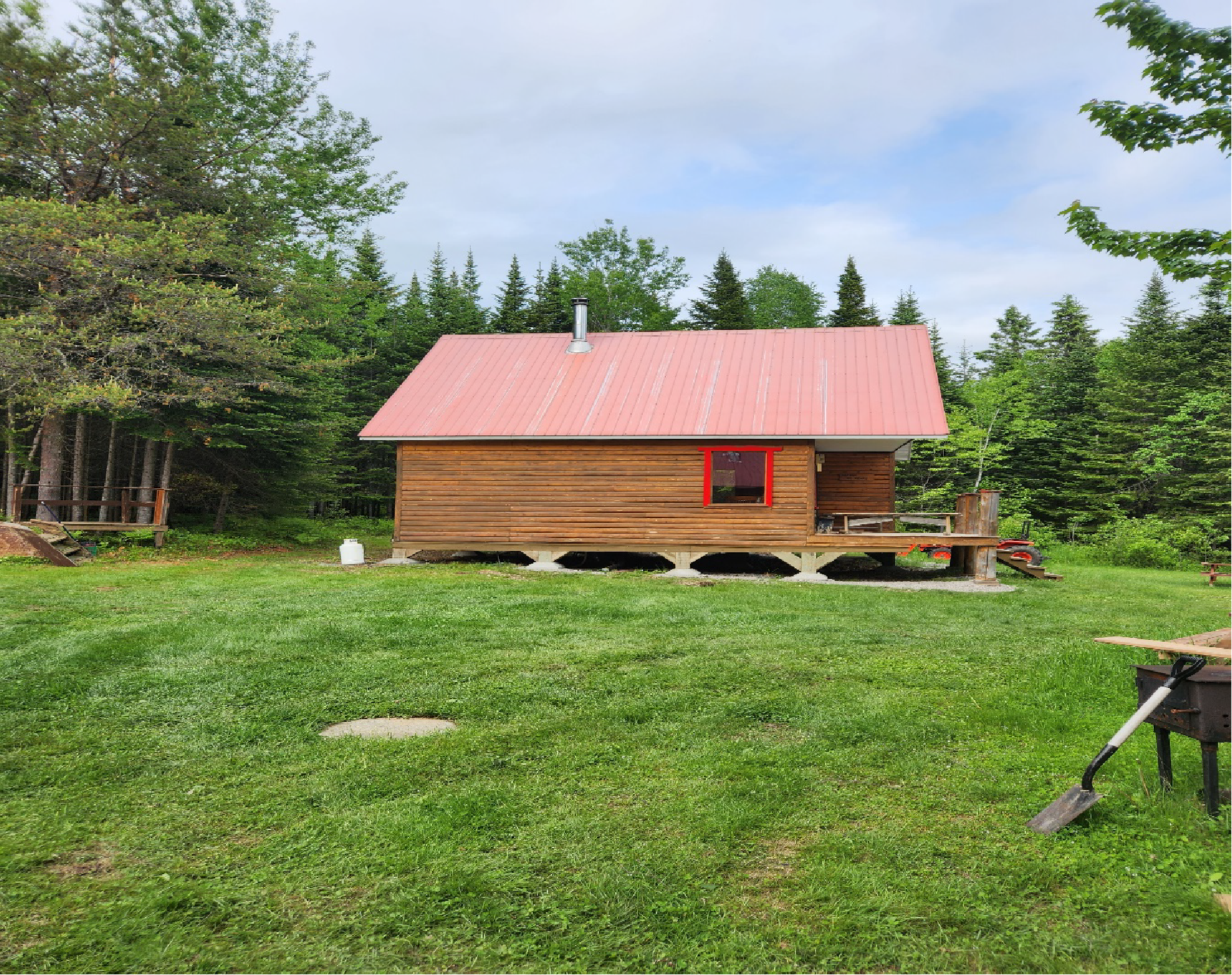 Une petite cabane en bois avec un toit rouge se trouve au milieu d'un champ herbeux.