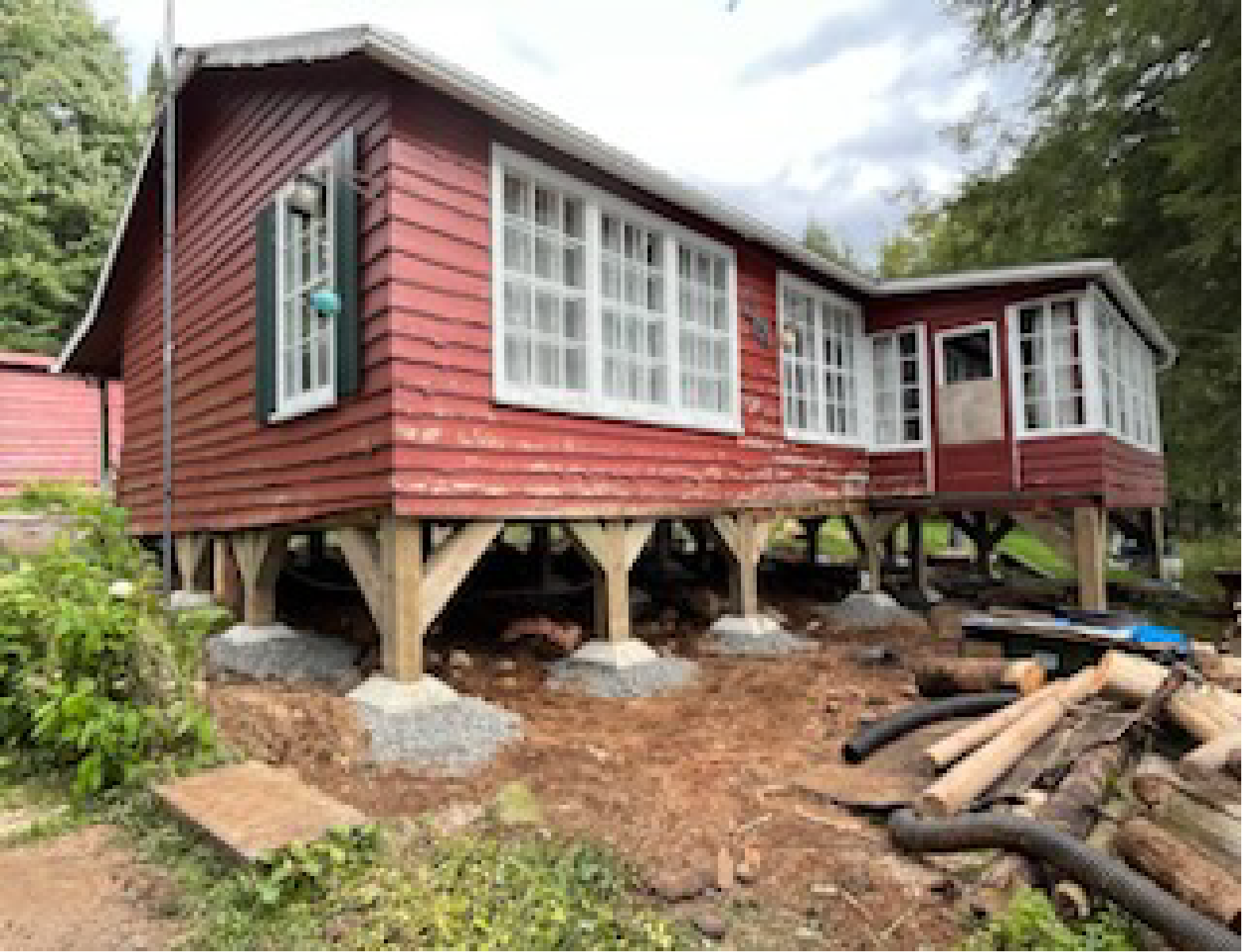 Une maison rouge est assise sur des pilotis au milieu d'un champ.