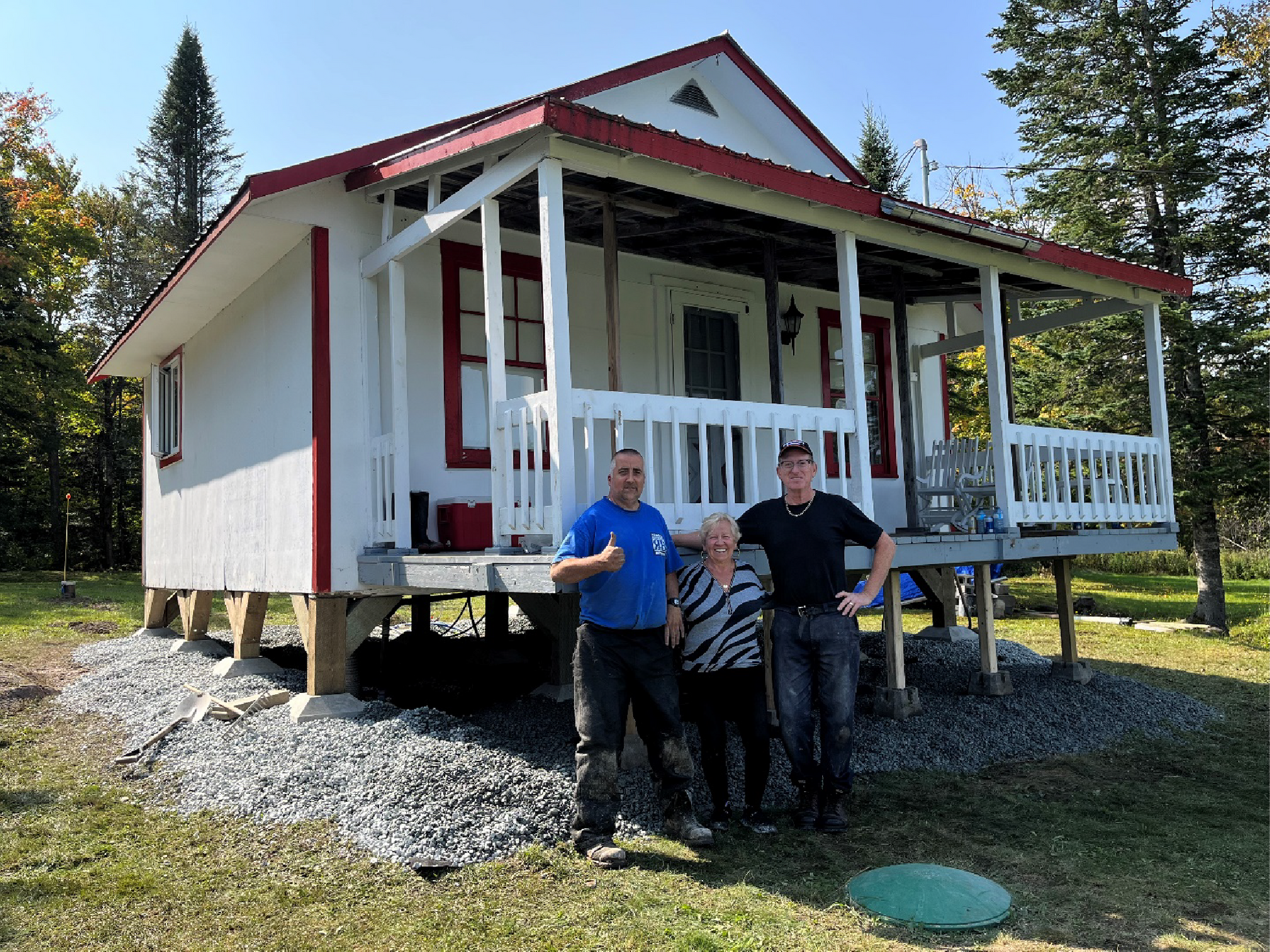Trois personnes se tiennent devant une petite maison blanche avec un porche.
