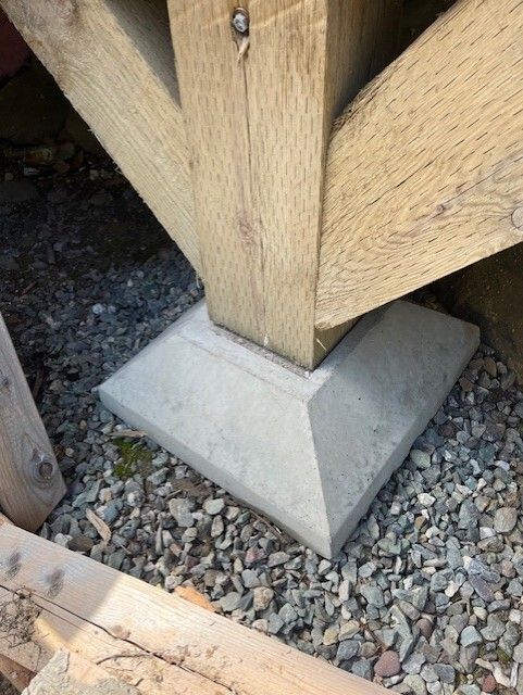 Poteau en bois sur une base en béton, posé sur du gravier.