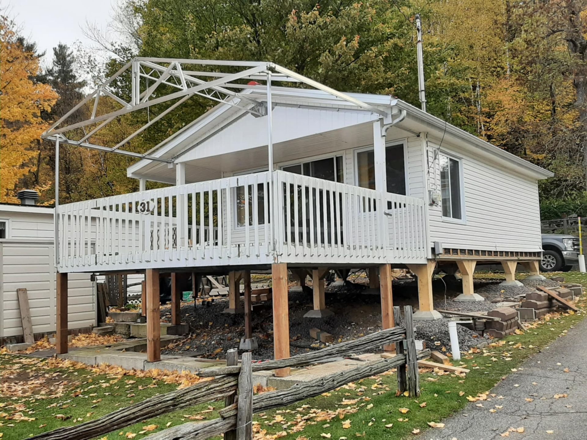 Maisonnette blanche surélevée avec un porche, soutenue par des poteaux en bois, dans une zone boisée.