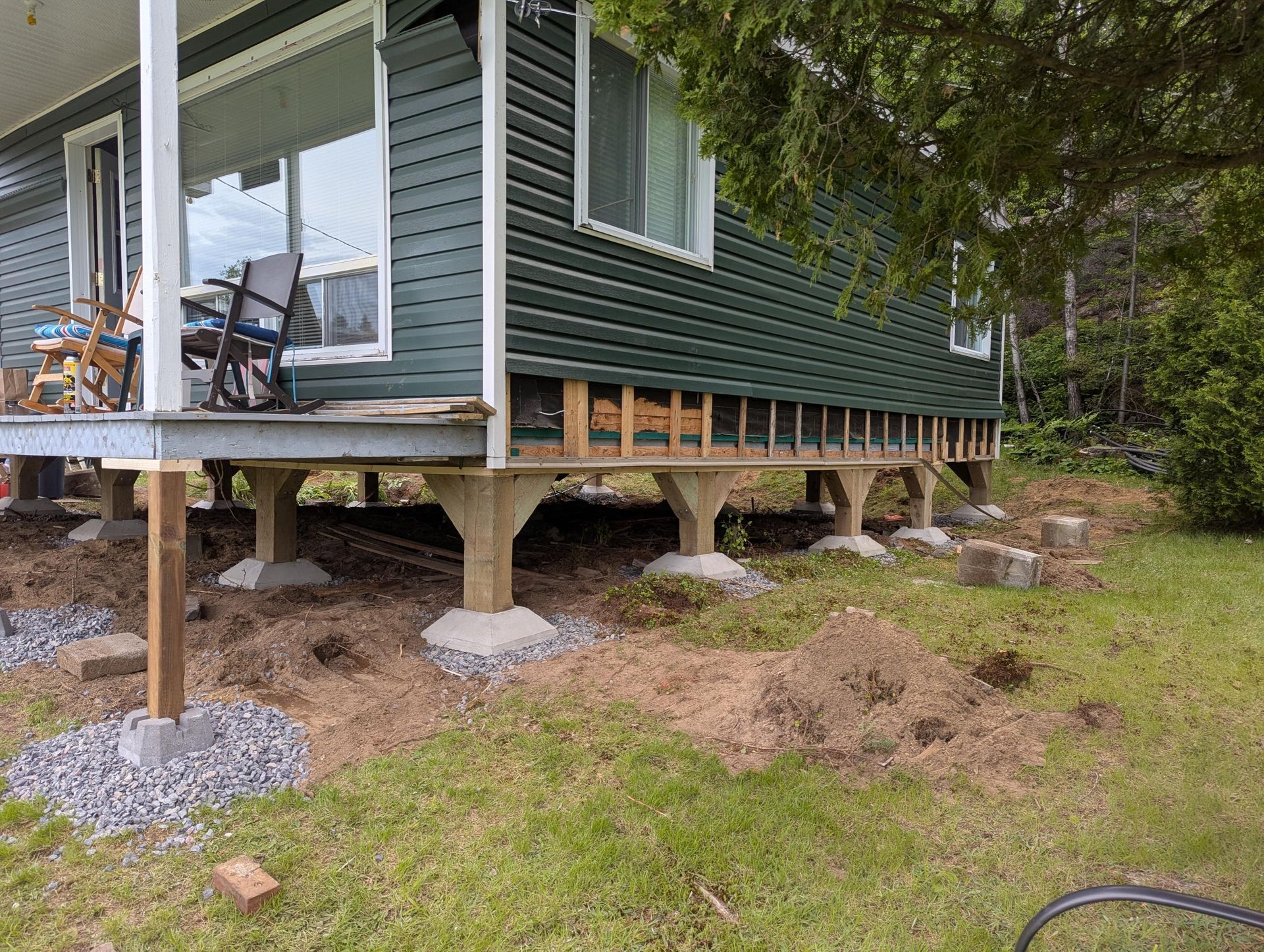 Réparation des fondations de la maison avec poutres en bois apparentes et supports en béton. Bardage et porche verts.