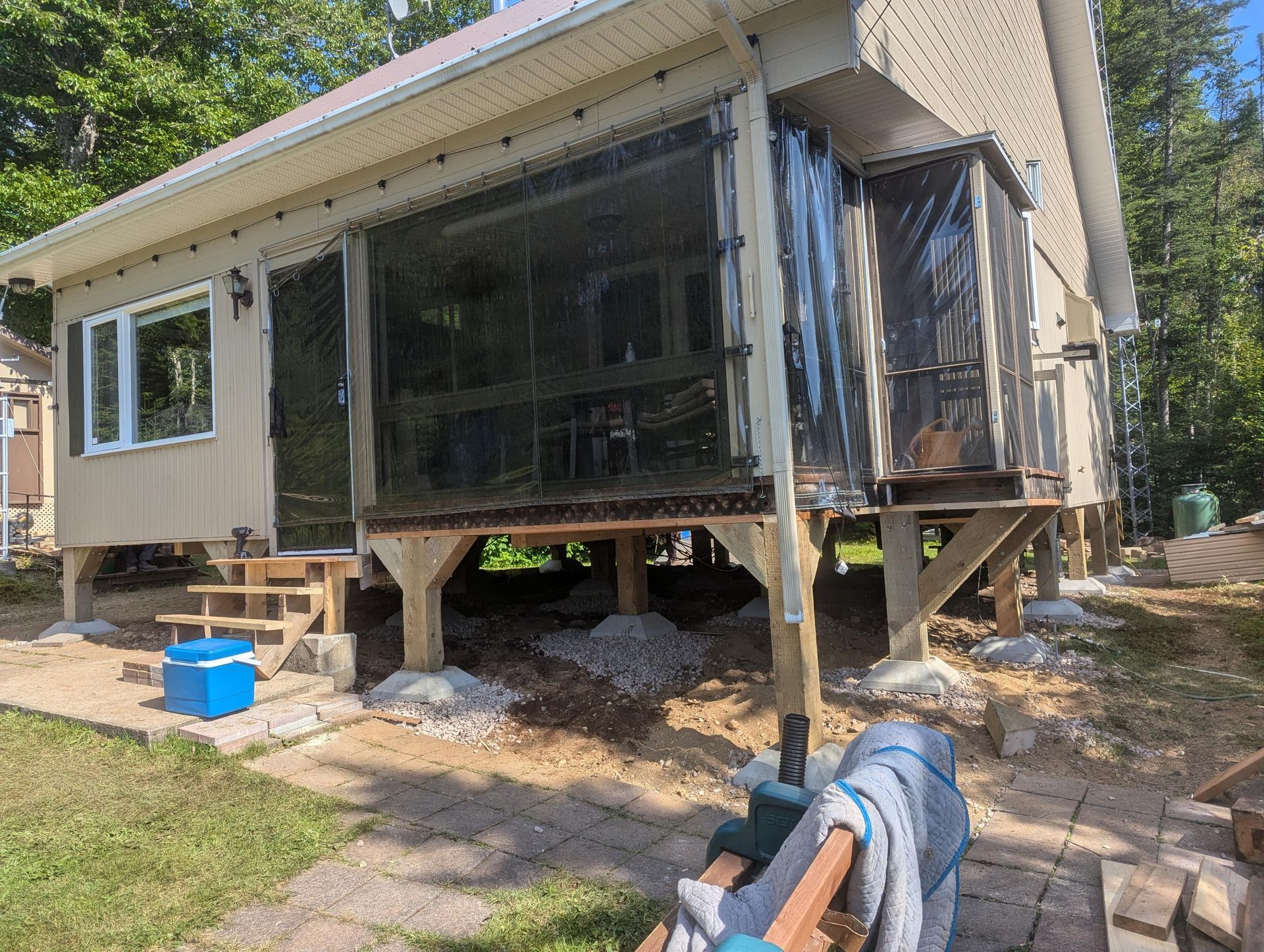 Ajout d'une véranda grillagée à une maison avec des supports en bois et un sol en gravier.