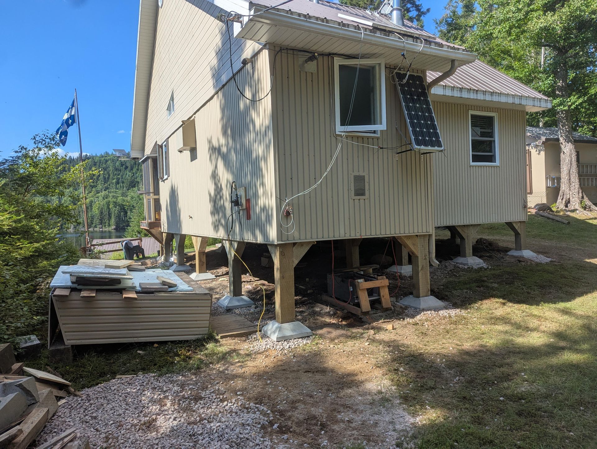 Maison sur pilotis, matériaux de construction à proximité. Un drapeau bleu flotte en arrière-plan. Cadre extérieur ensoleillé.