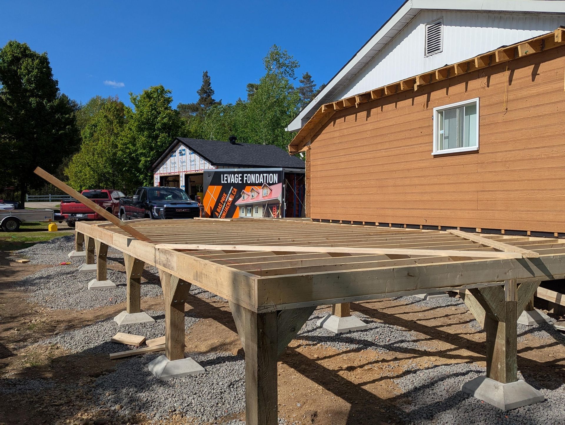 Terrasse en bois en construction à côté d'une maison et d'un garage ; cadre extérieur ensoleillé.