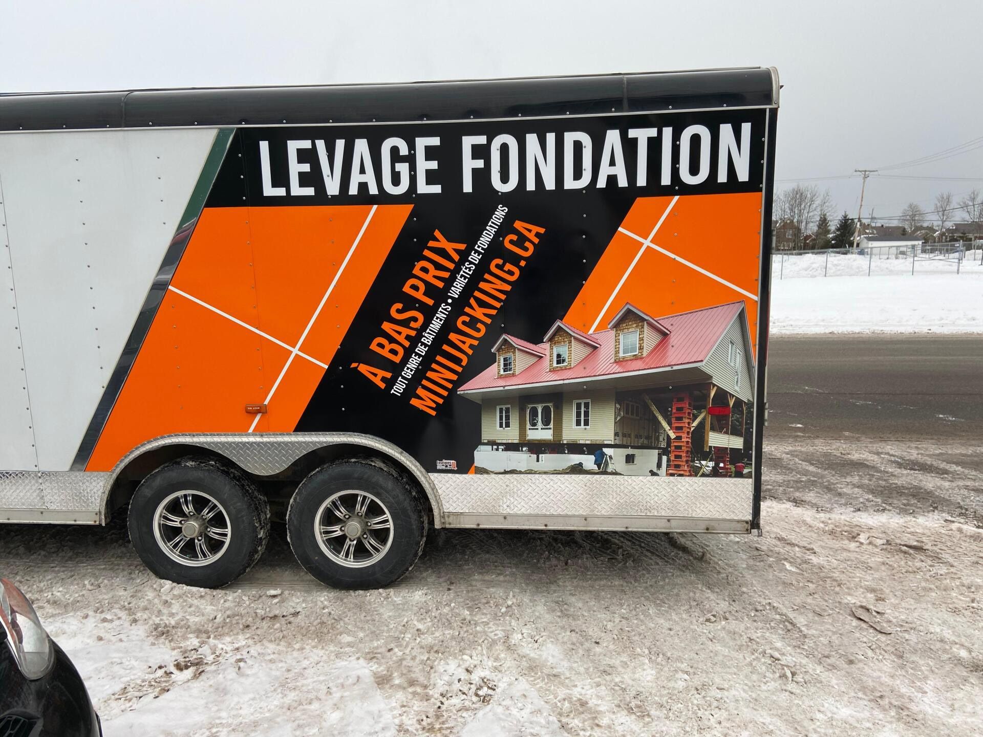 Remorque avec publicité pour levage de fondation, couleurs orange et noir, décor enneigé.