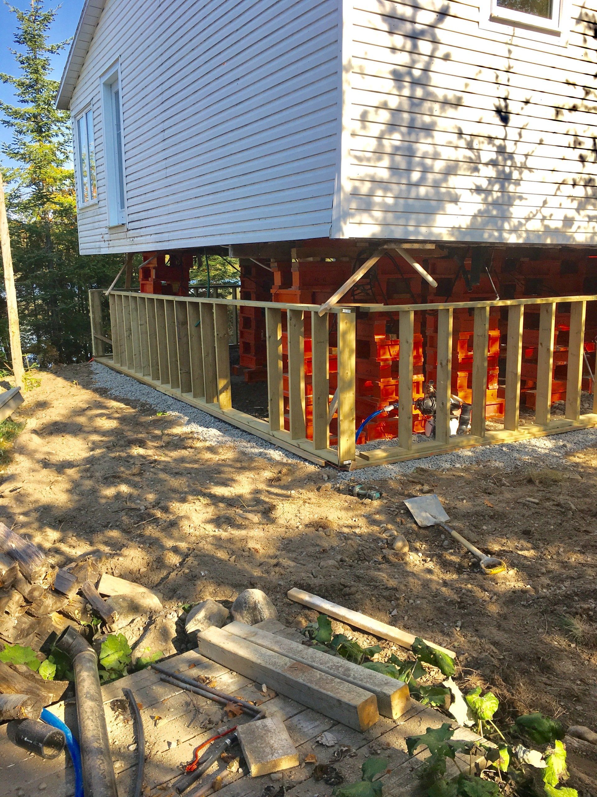 Une maison blanche est en cours de construction sur pilotis avec une terrasse en bois.