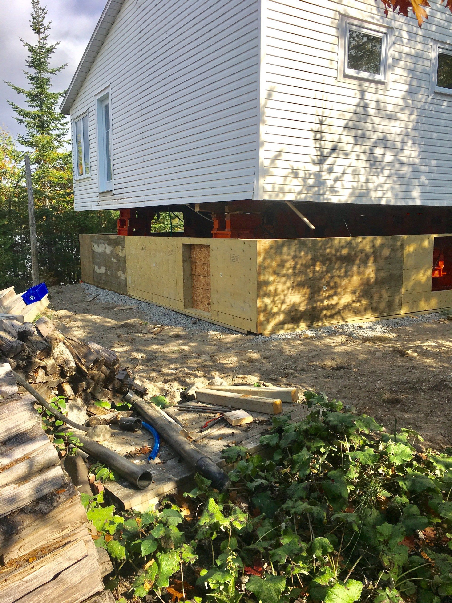 Une maison blanche est en train d'être construite sur pilotis dans la terre.