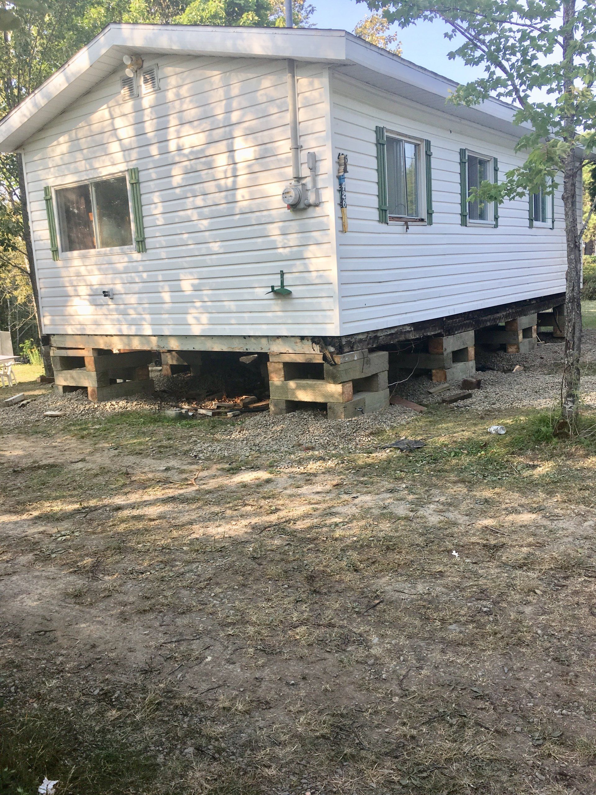 Une petite maison blanche est posée sur des pilotis au milieu d'un champ de terre.
