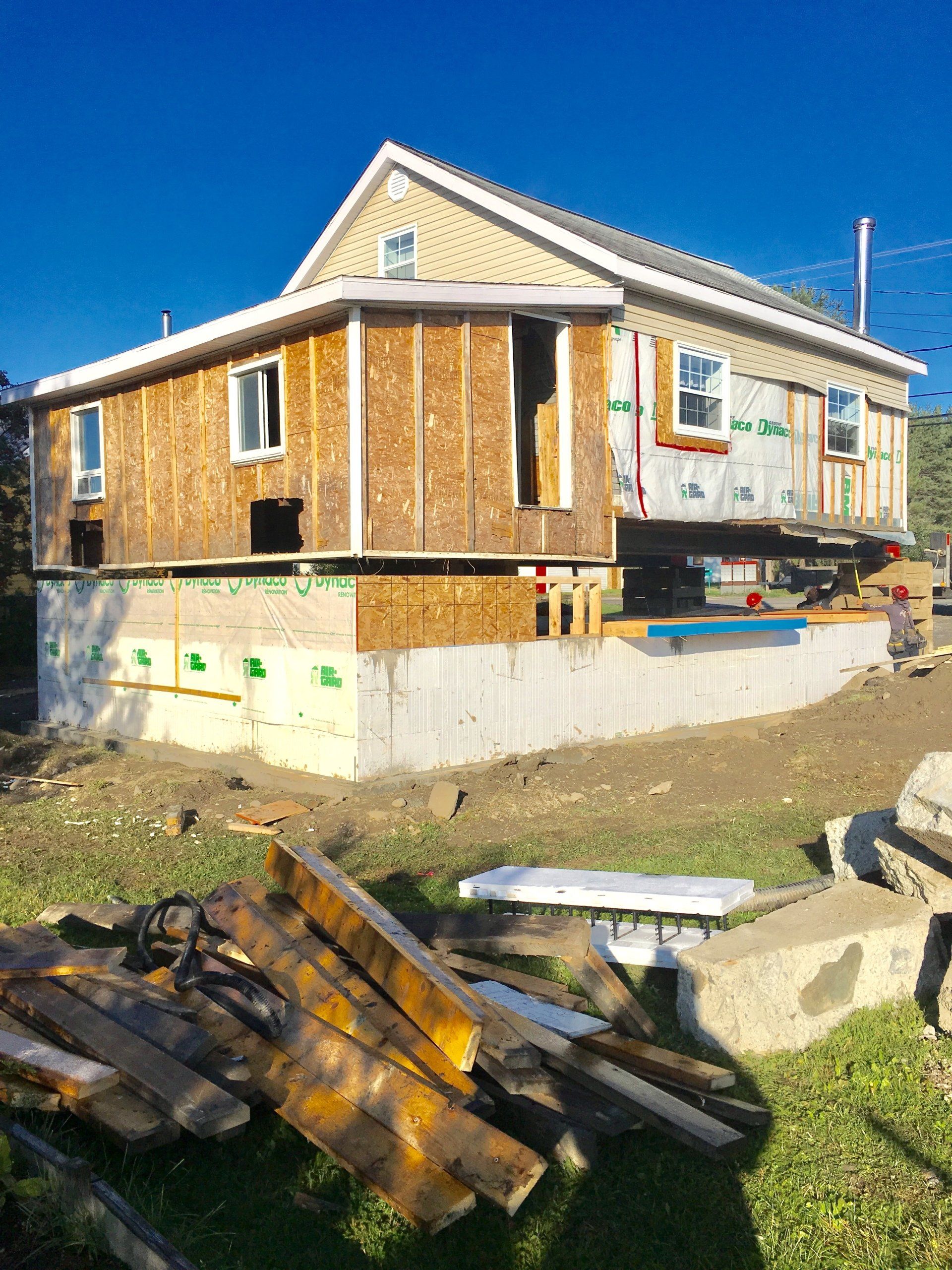 Une maison est en train d'être construite sur pilotis et un tas de bois se trouve devant elle.
