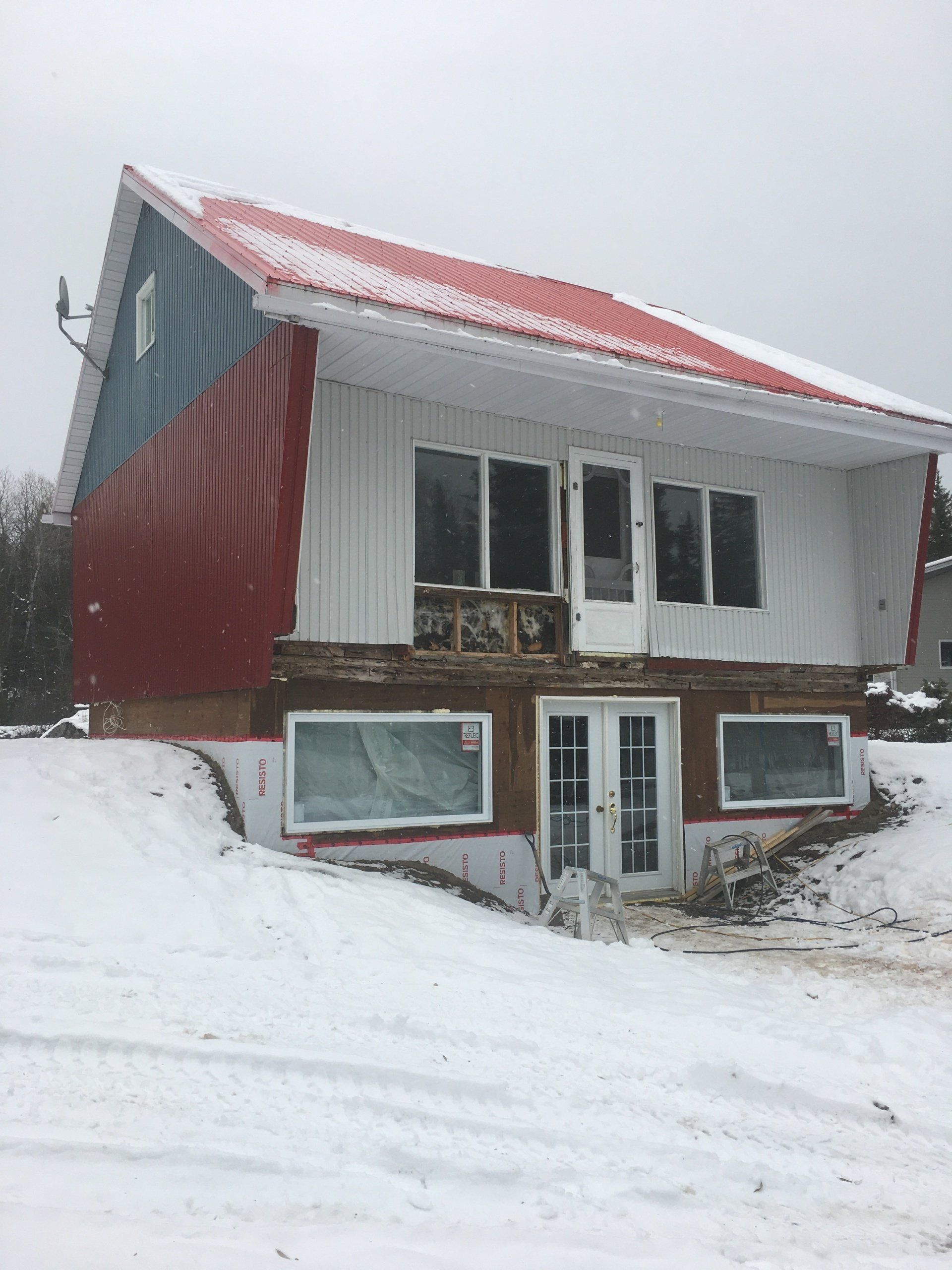 Une maison rouge, blanche et bleue avec un toit rouge est recouverte de neige.
