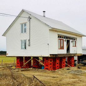 Une maison blanche est posée sur des briques rouges dans un champ.
