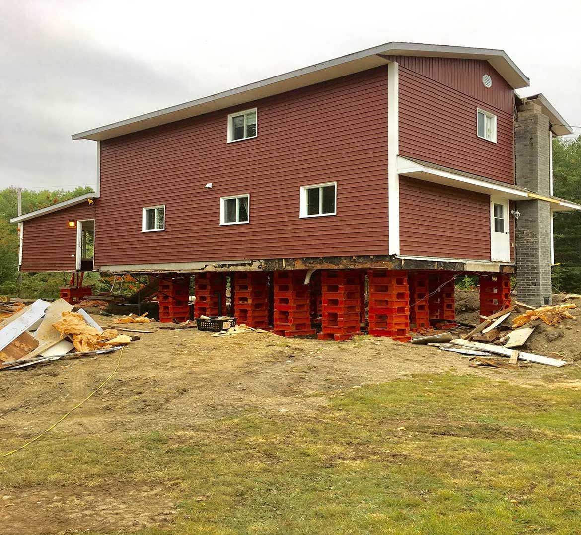 Une grande maison rouge est assise sur des pilotis dans un champ herbeux.