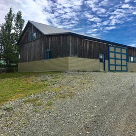 Une grande grange en bois avec une porte bleue se trouve au sommet d'un chemin de gravier.