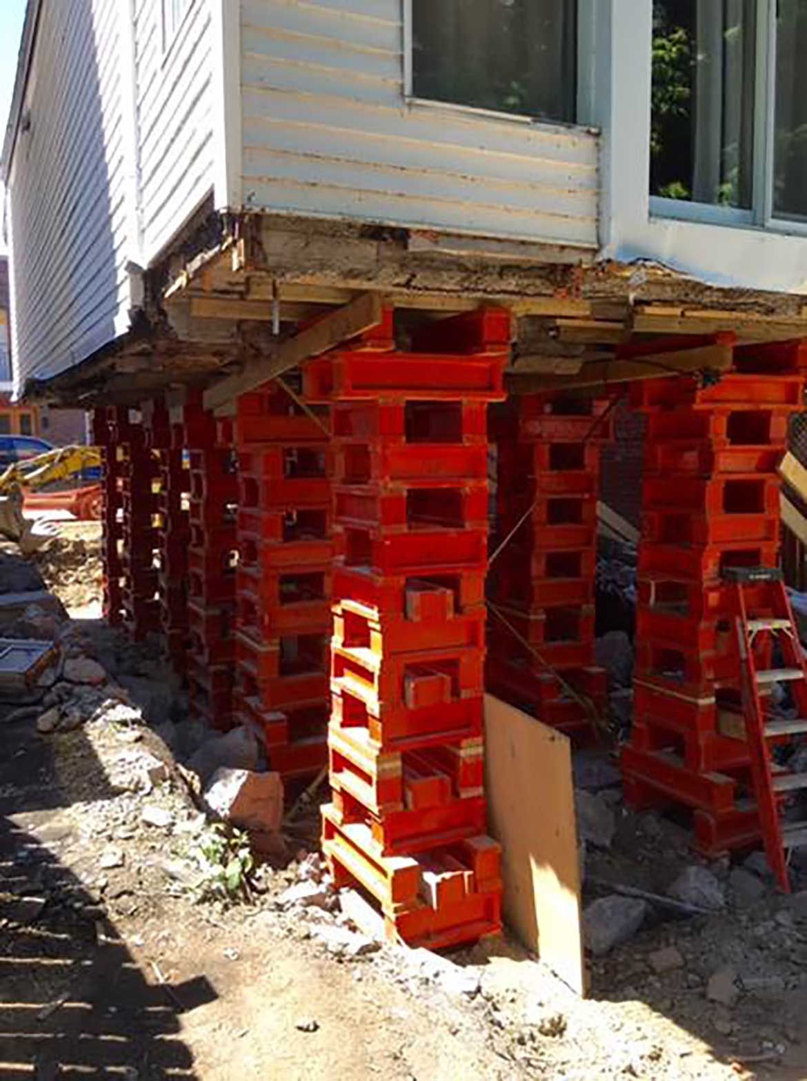 Une maison est en construction sur pilotis avec des briques rouges.