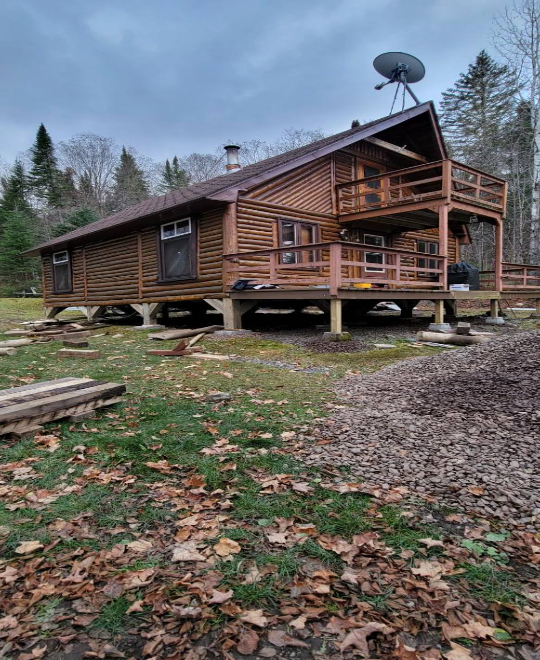 Une cabane en rondins avec une antenne parabolique sur le toit se trouve au milieu d'un champ.