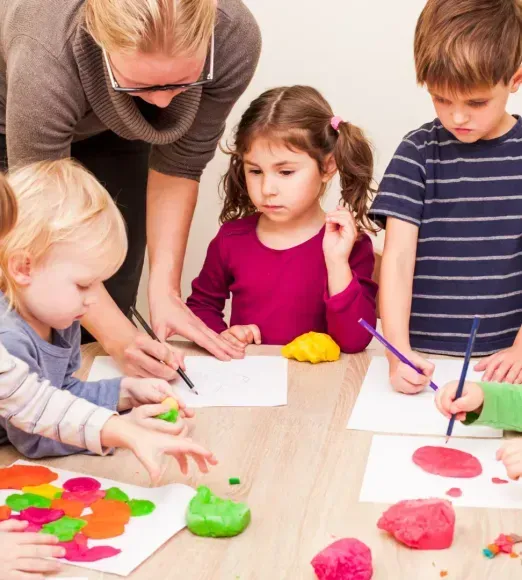 A group of children are sitting around a table playing with play dough.