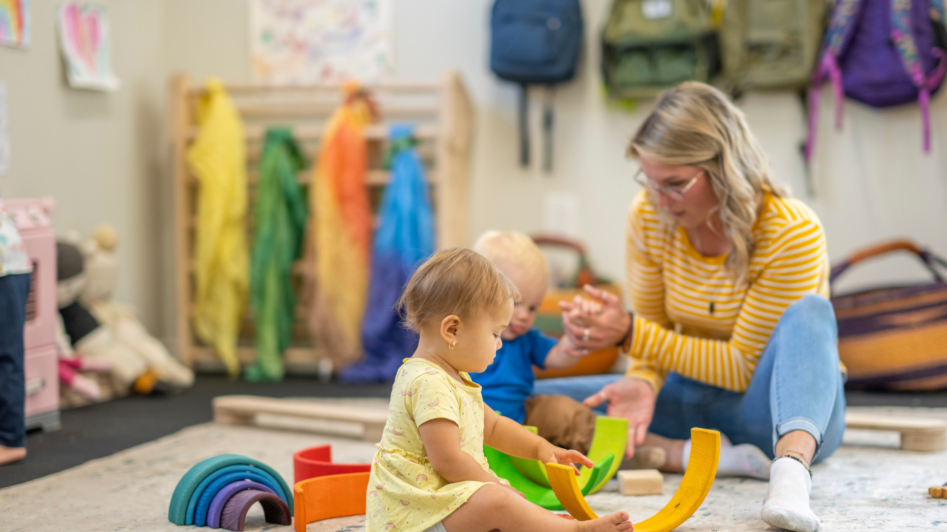 A woman is sitting on the floor playing with two children.