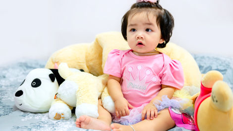 A baby girl is sitting on a bed next to a stuffed animal.
