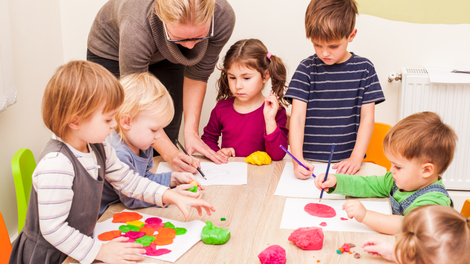 A group of children are sitting around a table playing with play dough.
